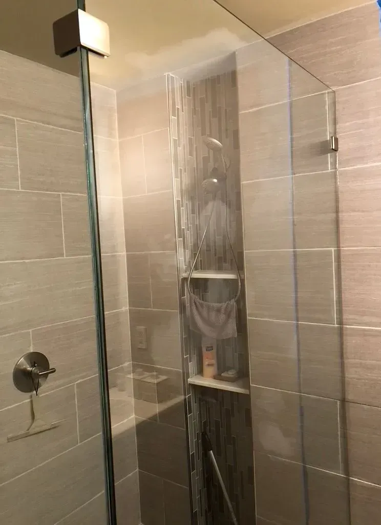 Glass shower enclosure with a shower curtain and beige tiled bathroom walls