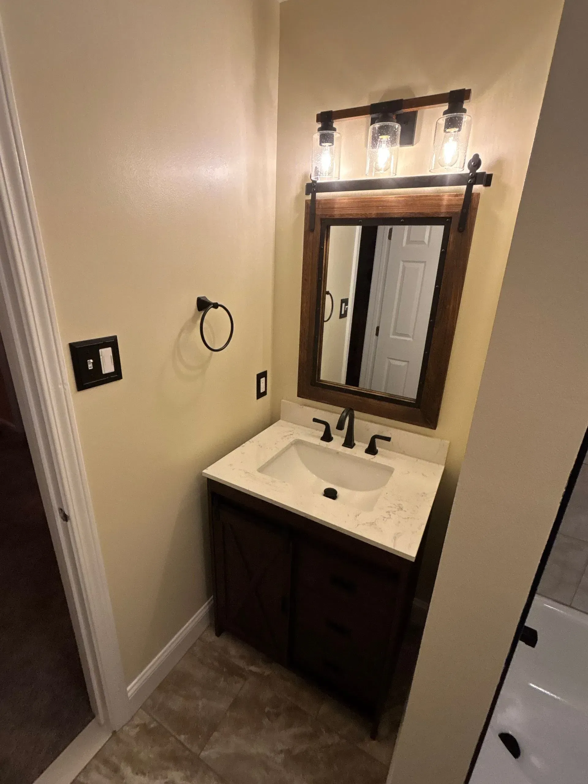 Small beige bathroom with vanity sink, mirror, and light fixture above.