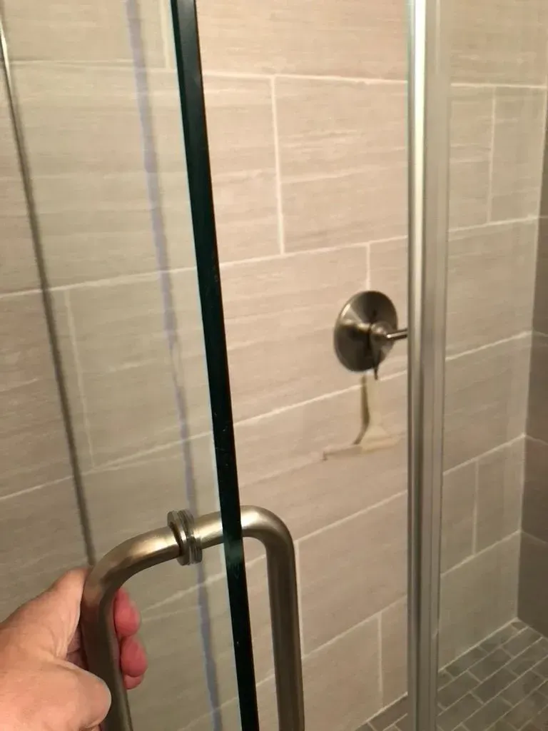 Hand holding a shower door handle next to a chrome shower control in a tiled bathroom