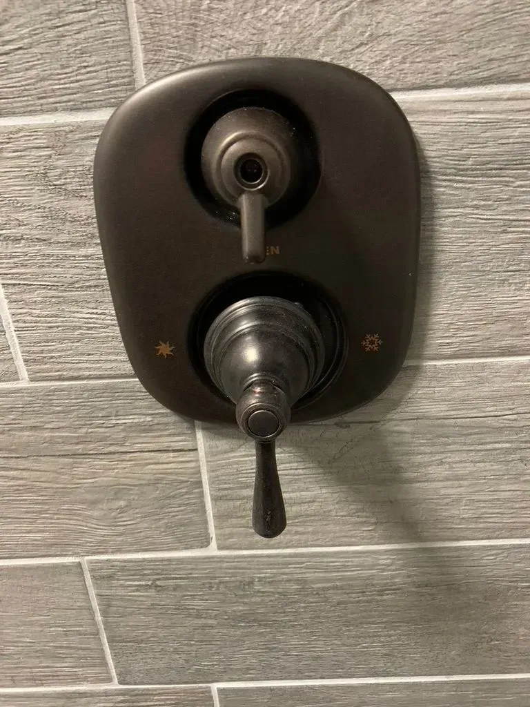 Wall-mounted shower control valve with two knobs on a tiled bathroom wall