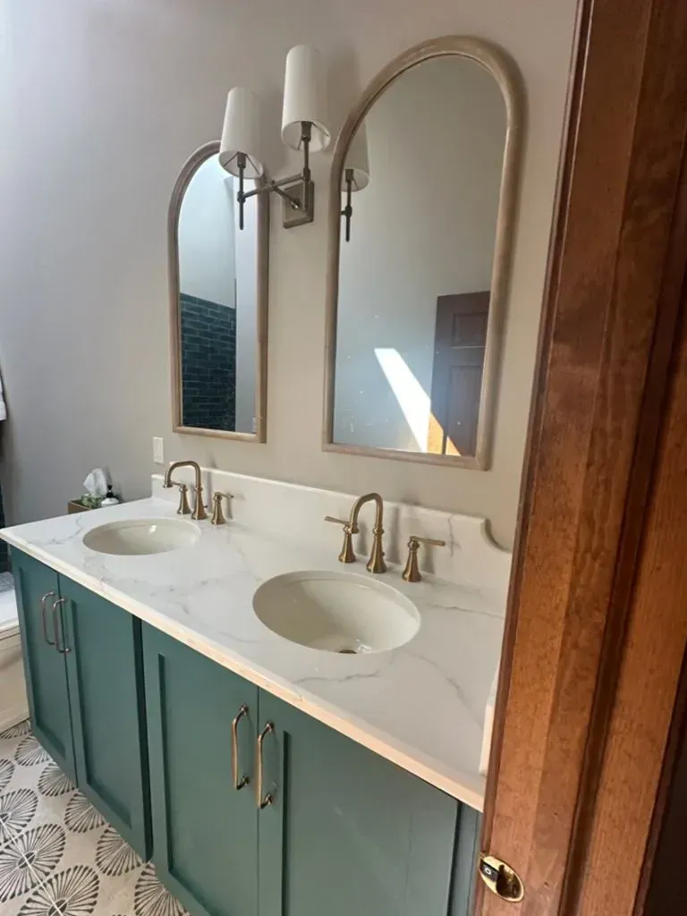 Bathroom vanity with double sinks, arched mirrors, teal cabinets, and brass faucets