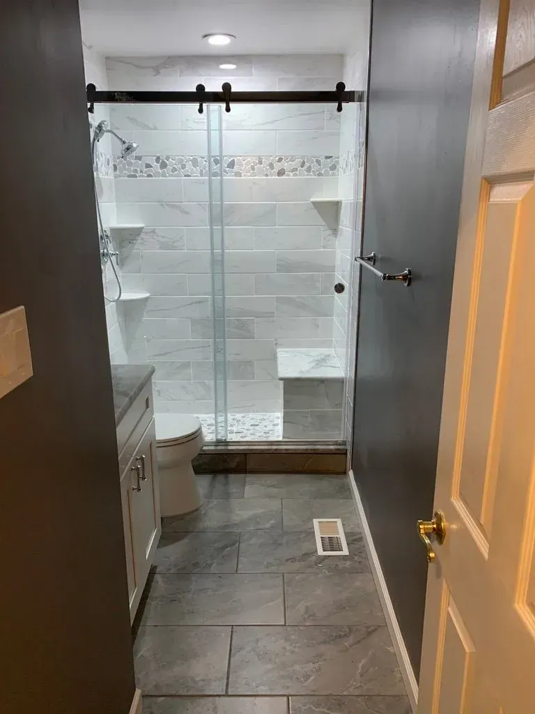 Small bathroom with a glass shower, dark tile floor, toilet, and open door.