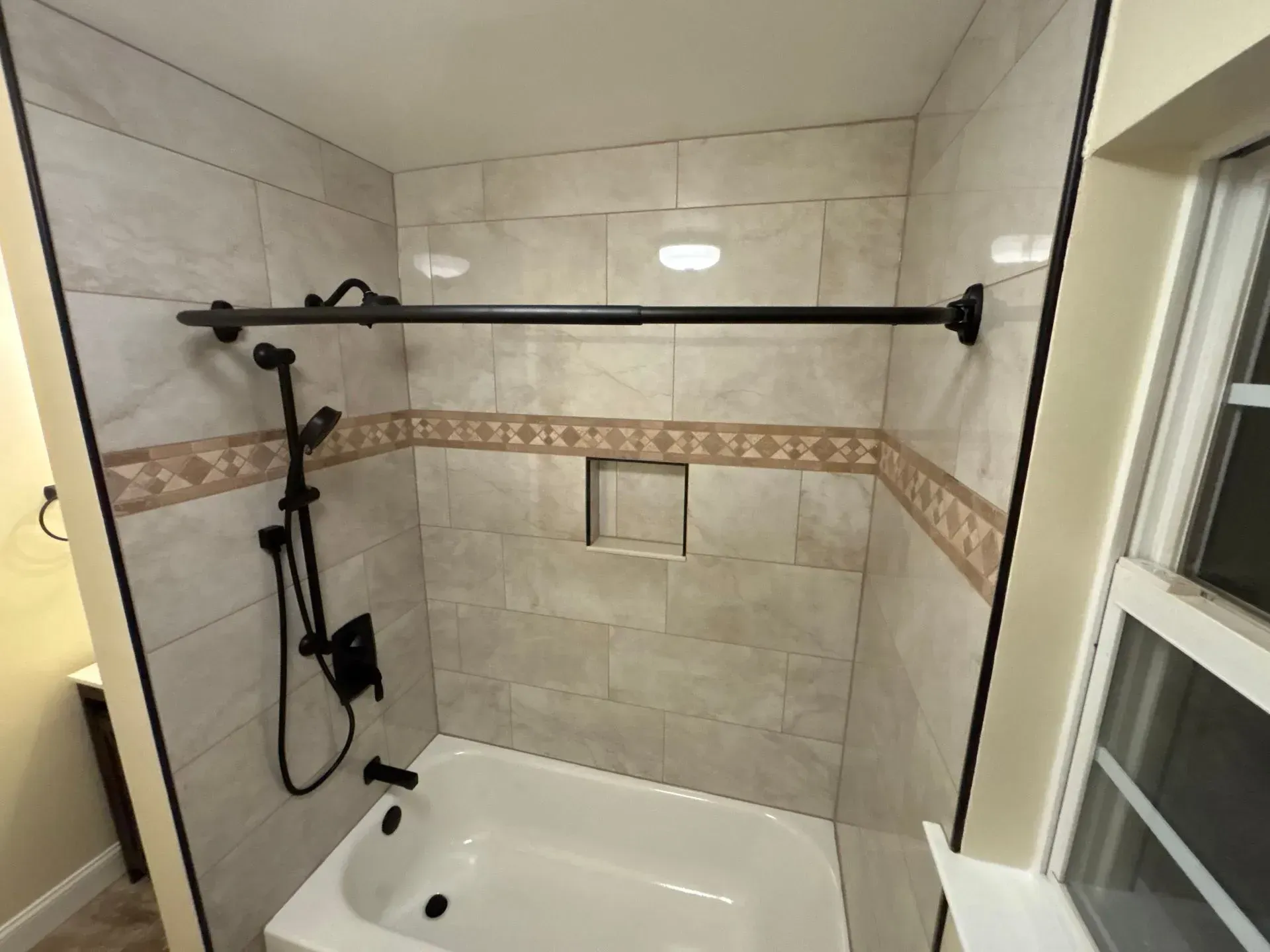 Accessible shower with grab bars, fold-down bench, showerhead, and beige tiled walls.