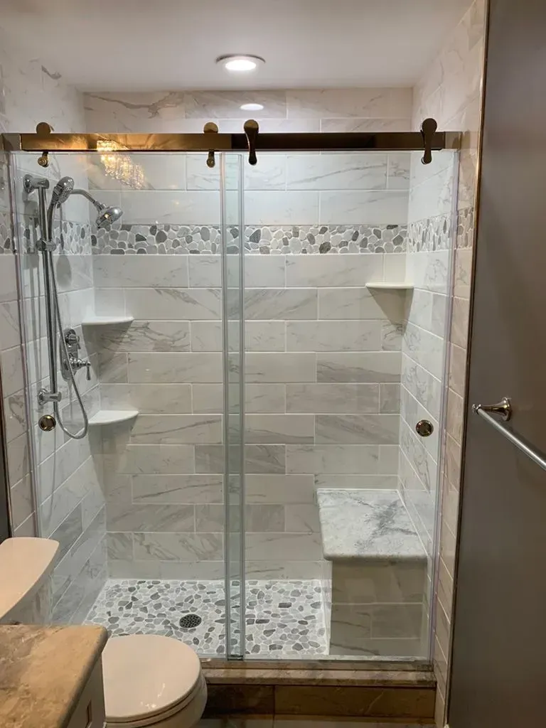 Modern tiled bathroom with a glass shower enclosure, mosaic floor, and built-in corner benches