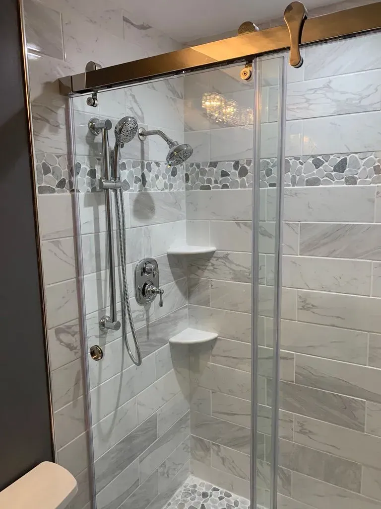 Glass shower stall with white tile walls, corner shelves, and a showerhead in a bathroom