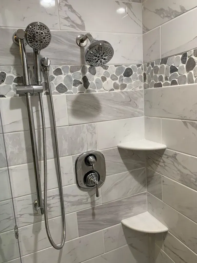 Tiled shower with dual showerheads, handheld sprayer, and corner shelves.