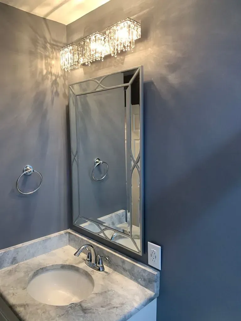 Bathroom vanity with marble sink, mirror, chrome faucet, and wall light above