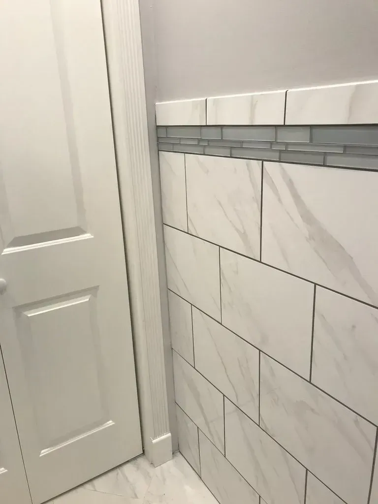 Bathroom corner with white tile wainscoting, gray accent trim, and a white door
