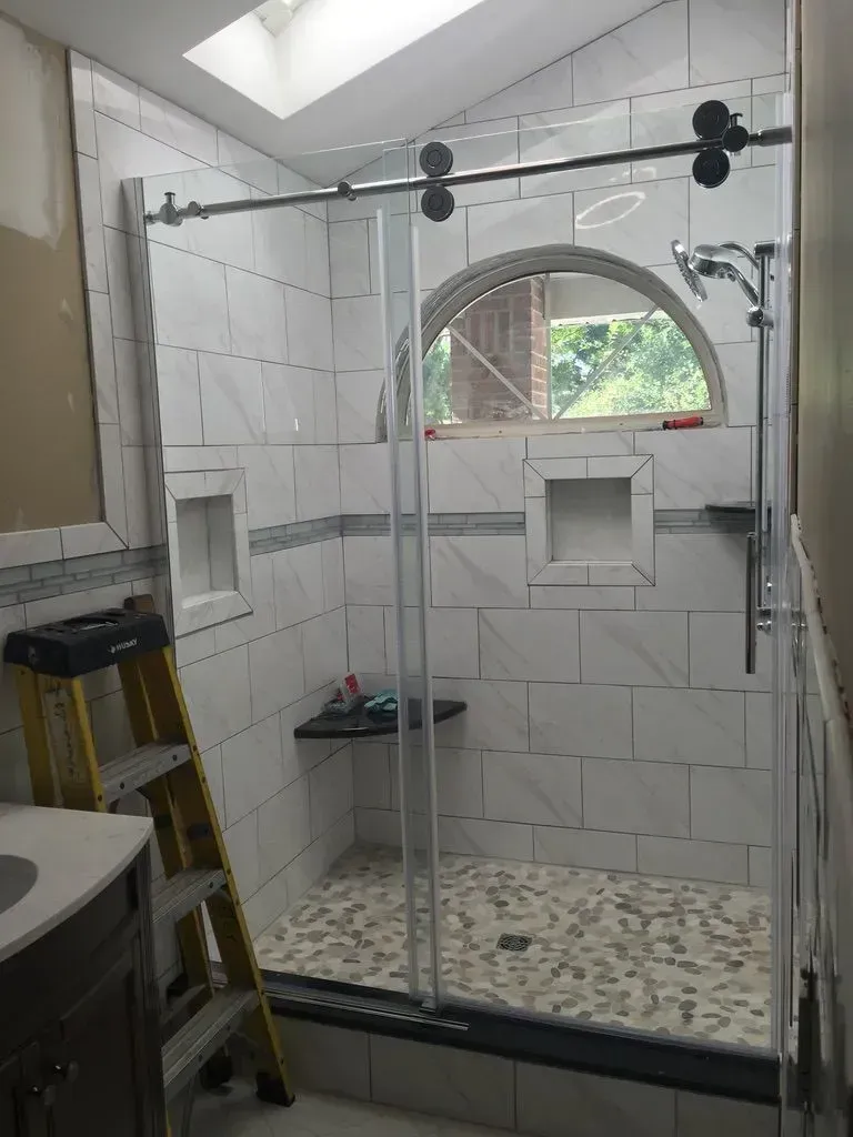 Bathroom with a glass shower enclosure, tiled walls, arched window, and a small stool inside.