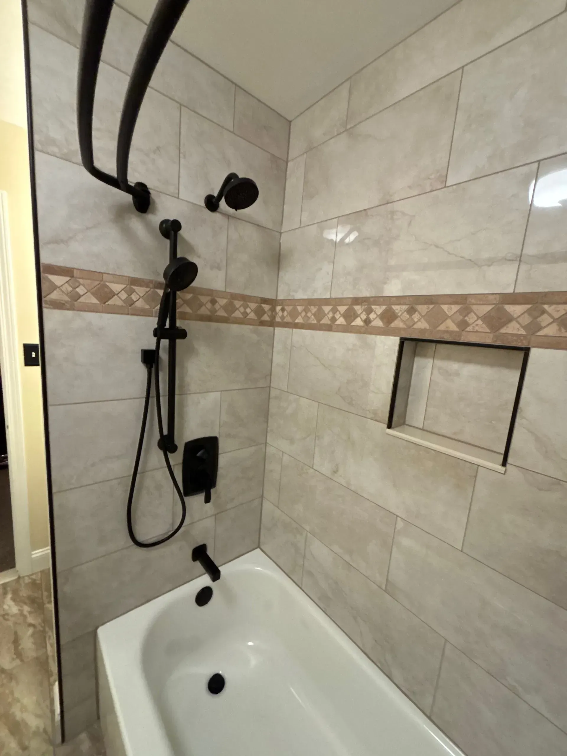 Accessible bathroom shower with grab bars, handheld showerhead, and a tub seat against beige tile walls