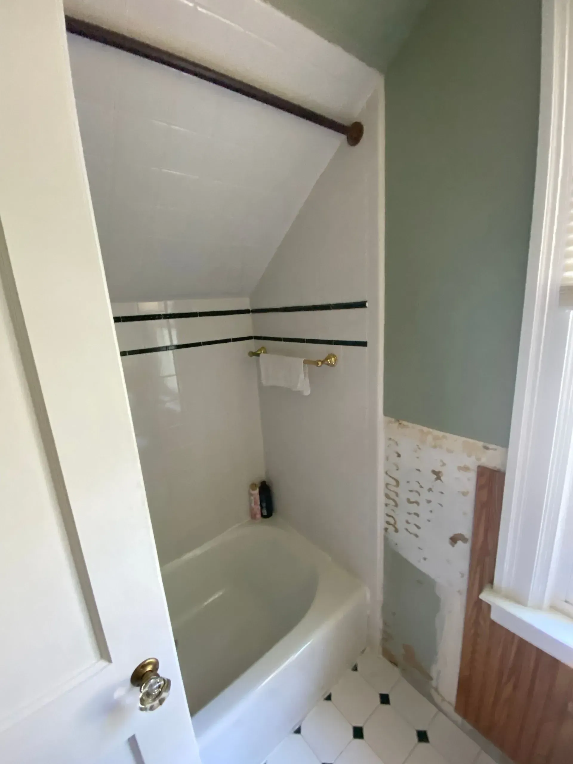 Narrow bathroom with a bathtub, white walls, and a slanted ceiling in a small alcove.