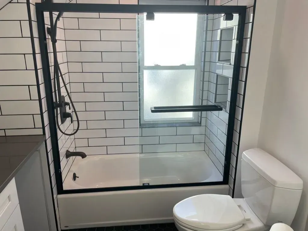 Modern bathroom with glass shower, white tile, and a toilet in the foreground