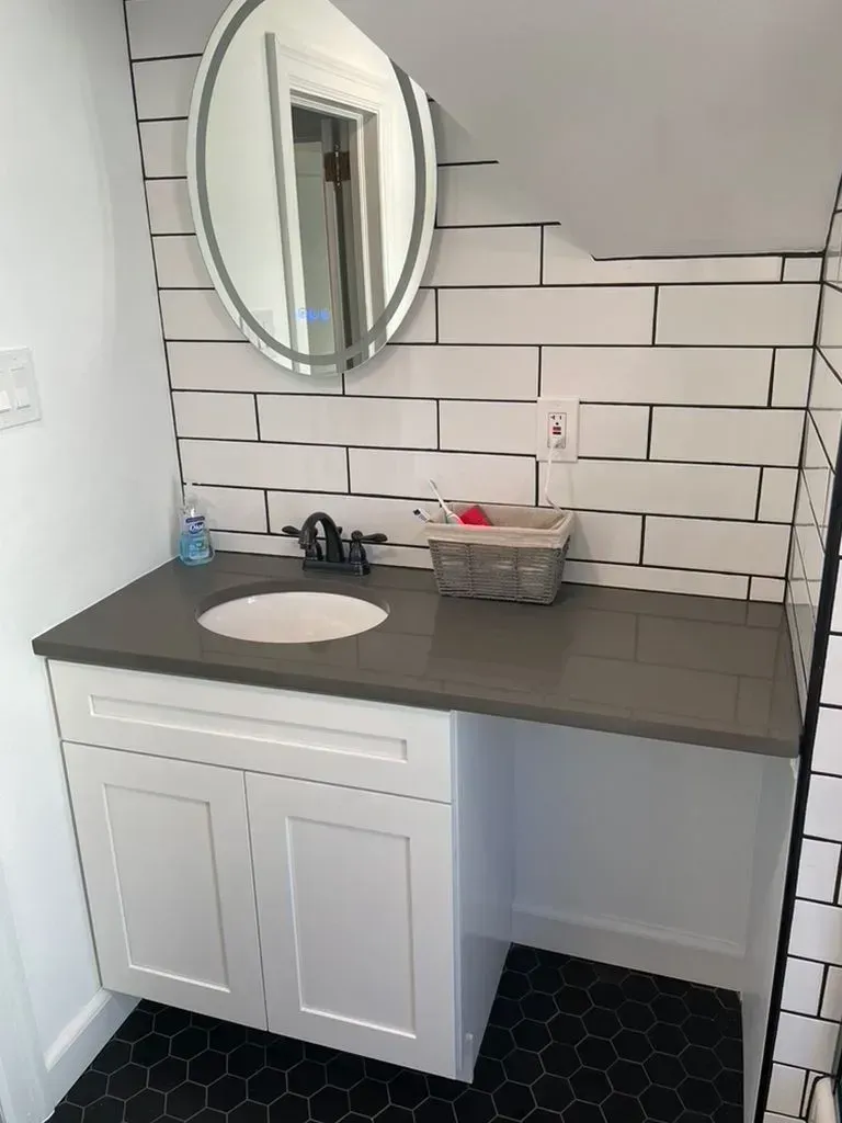 Modern bathroom vanity with round mirror, white sink, gray countertop, and subway tile backsplash