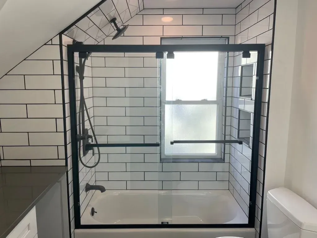 Glass walk-in shower with black frame, white subway tile, handheld shower, and frosted window.