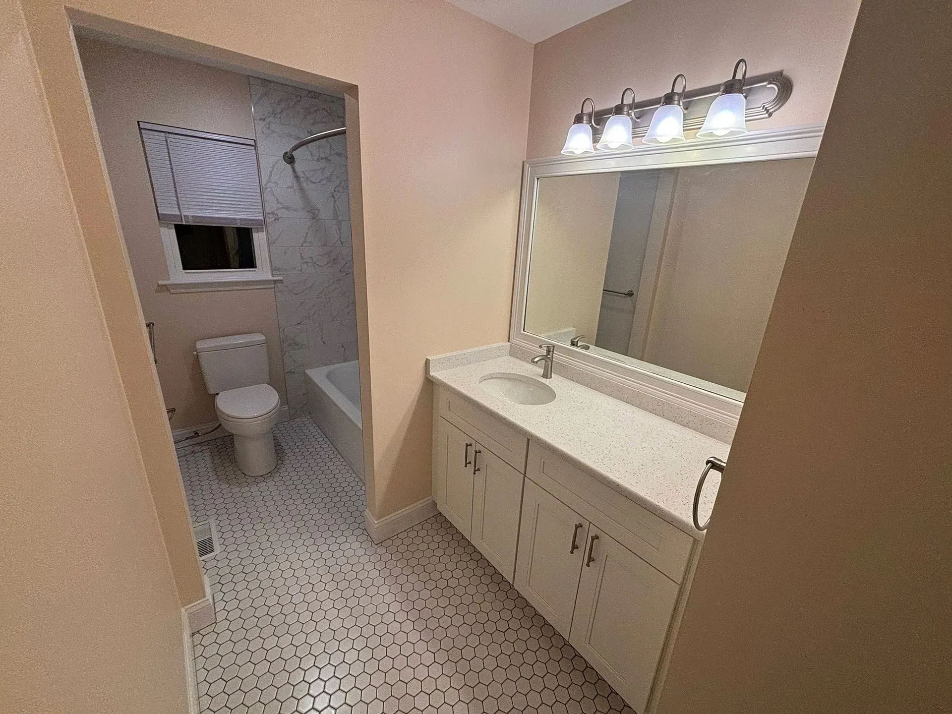 Small bathroom with tiled floor, toilet, bathtub, and vanity with large mirror under bright lights