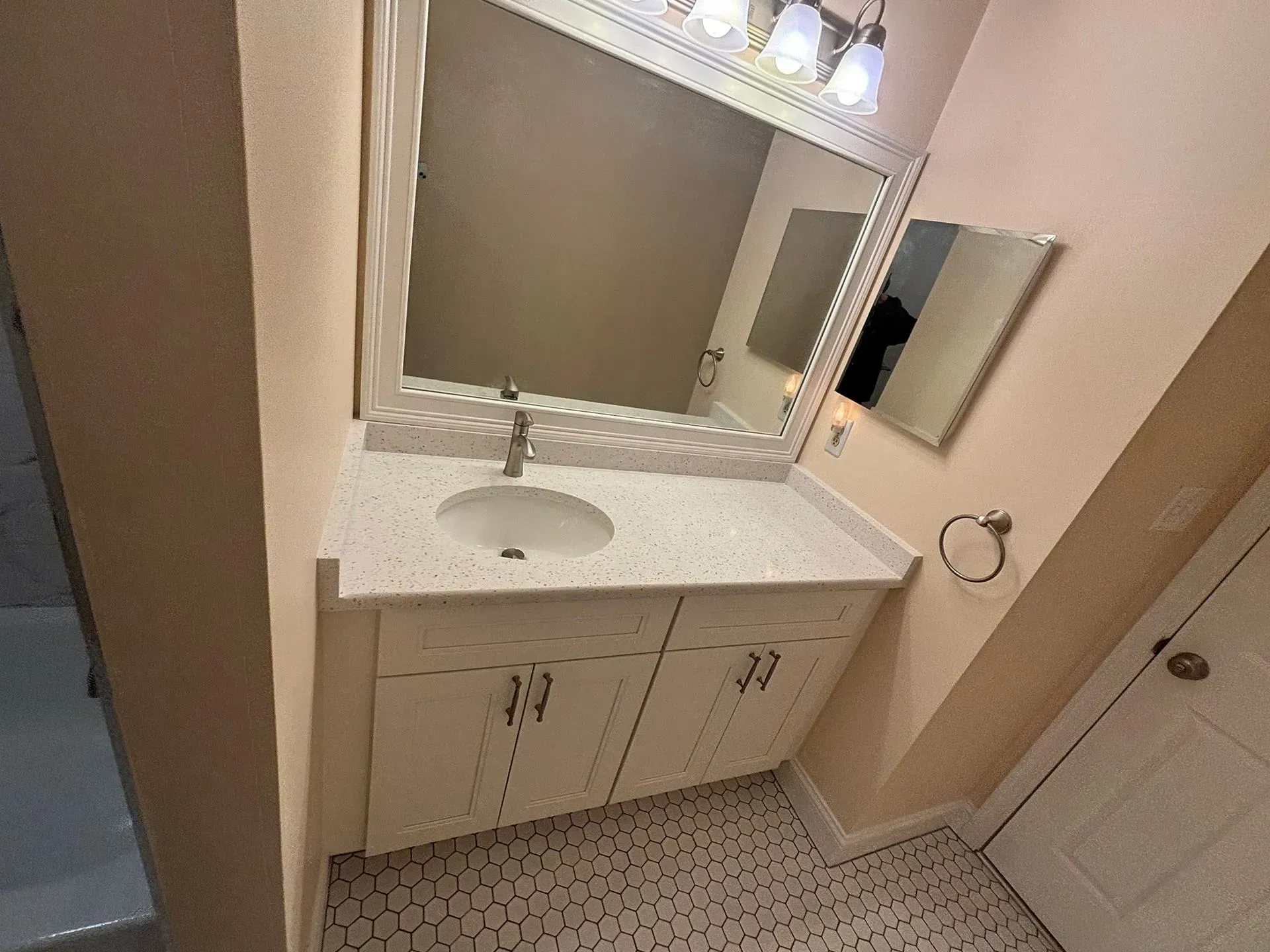 Bathroom vanity with large mirror, white sink, beige walls, and tiled floor under bright lights