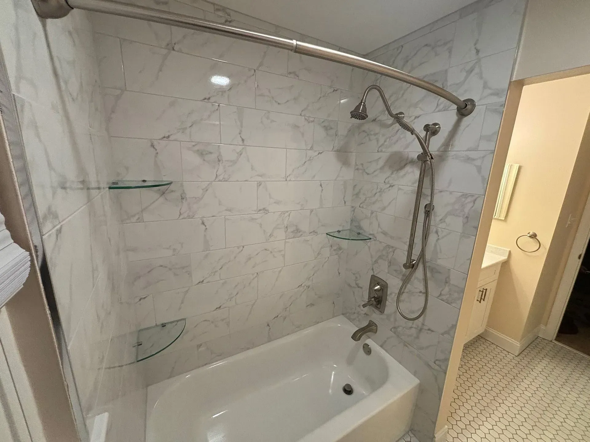 Accessible bathroom with marble-tiled shower, grab bars, and a bathtub with handheld showerhead.
