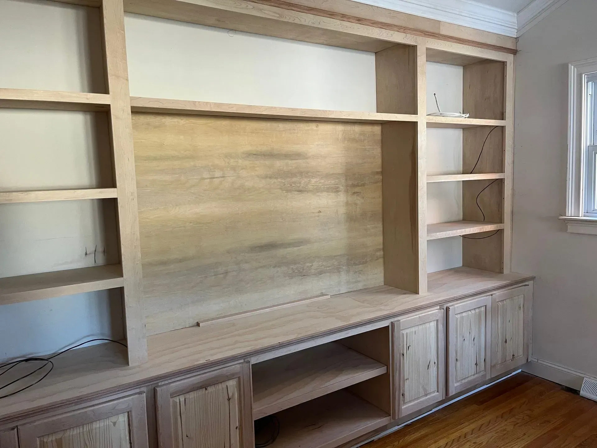 Built-in wall entertainment center with open shelves, cabinets, and a wood backing panel in a bright room