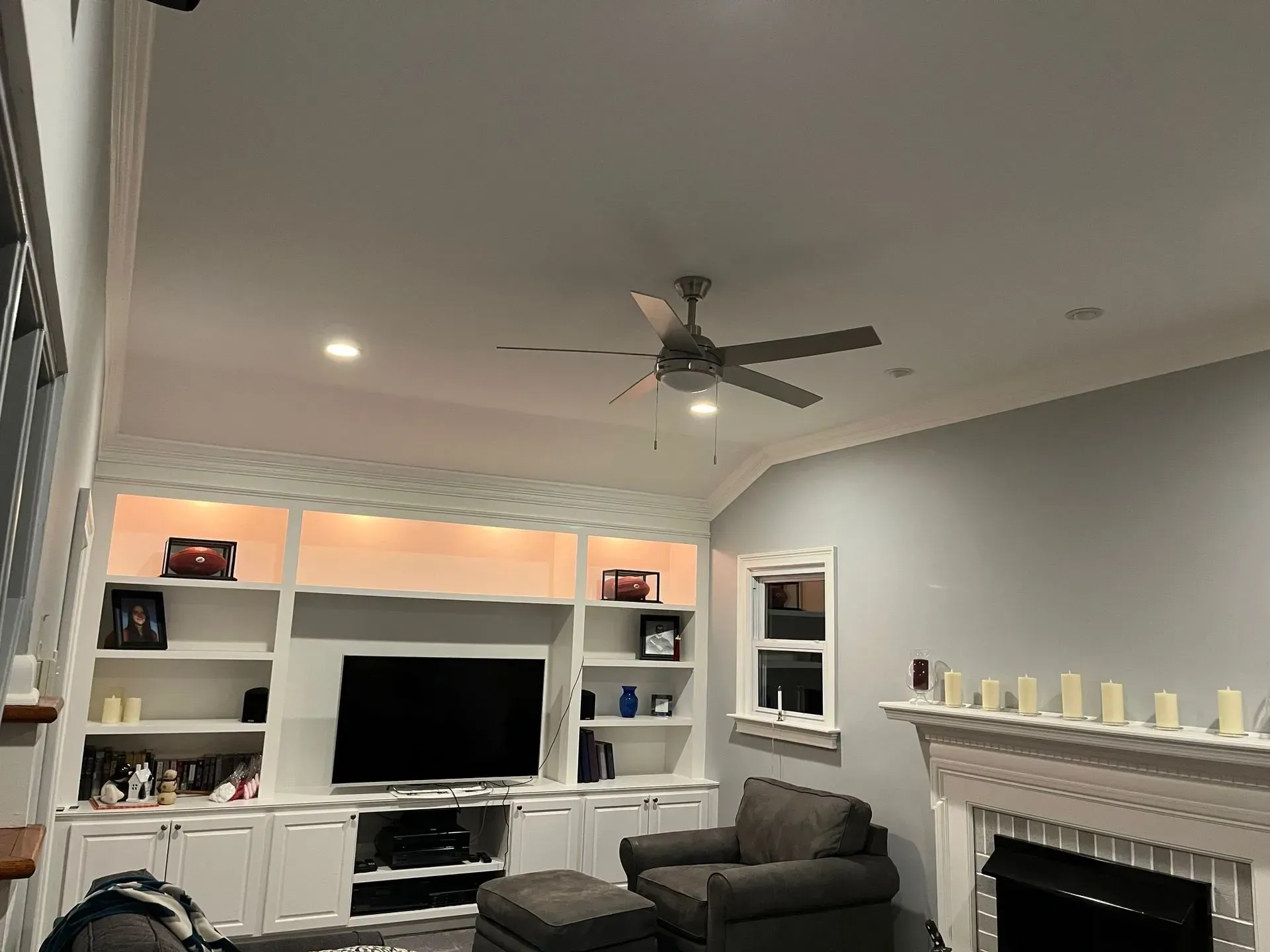 Living room with white built-ins, TV, gray chair, fireplace, and ceiling fan on gray walls