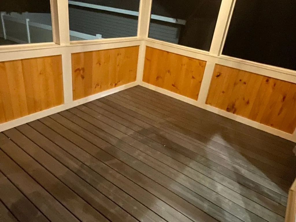 Wooden deck with railing and windows at night, lit by warm indoor light