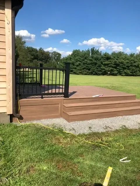 Backyard deck with black gate, wooden steps, and green lawn under a blue sky