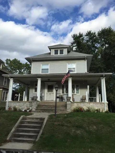 Two-story white house with front porch, American flag, and stairs leading up from the lawn