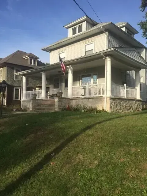 Victorian-style house with a porch, white trim, and an American flag on a sunny day