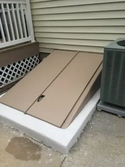 Tan rooftop hatch with pull handle beside house siding and air conditioner unit