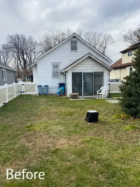 Backyard with patchy grass, white house, sliding glass doors, and a black bucket in the center