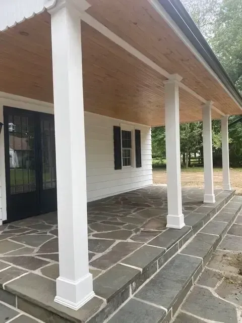 White porch with columns and stone walkway beside a building, viewed at an angle.
