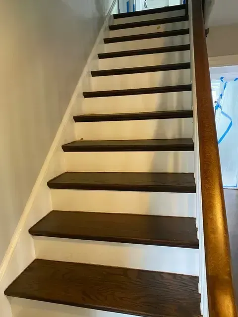 Indoor staircase with dark wood steps, white risers, and a wooden handrail against cream walls.