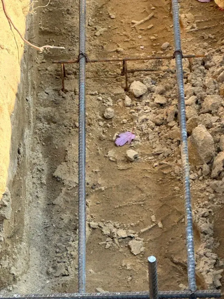 Dirt trench wall with two vertical rebar rods and a small purple object in the soil