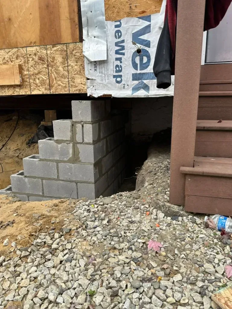 Concrete block stairway beside a boarded-up doorway on a gravel pile under construction.