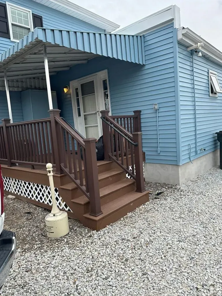Blue house with small front porch, brown steps and railing, and gravel yard.