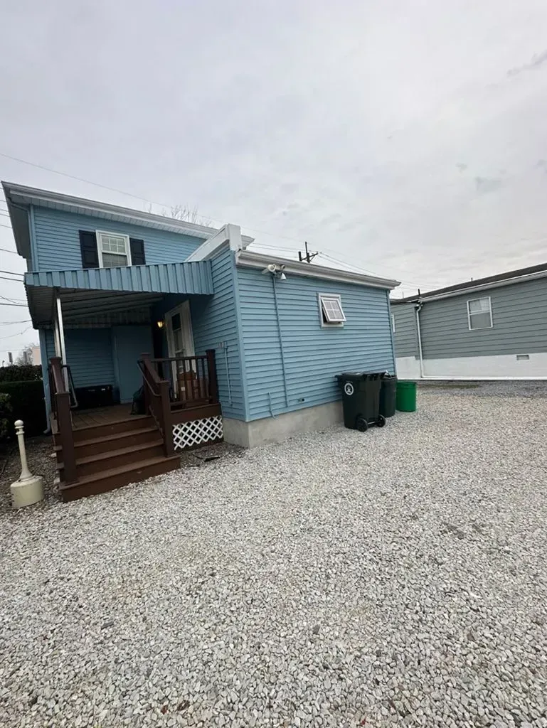 Blue house with porch and gravel yard under an overcast sky