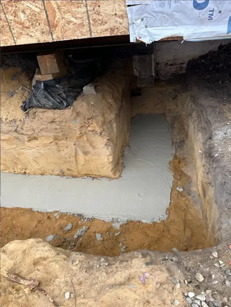 Excavation pit with exposed soil and a small concrete-filled section beneath a structure