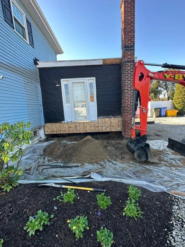 Backhoe beside a house lifting a small deck during outdoor demolition work
