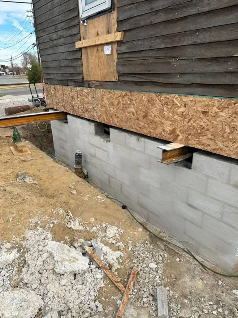 Exterior house renovation with OSB sheathing over a cinder block foundation and dirt ground below