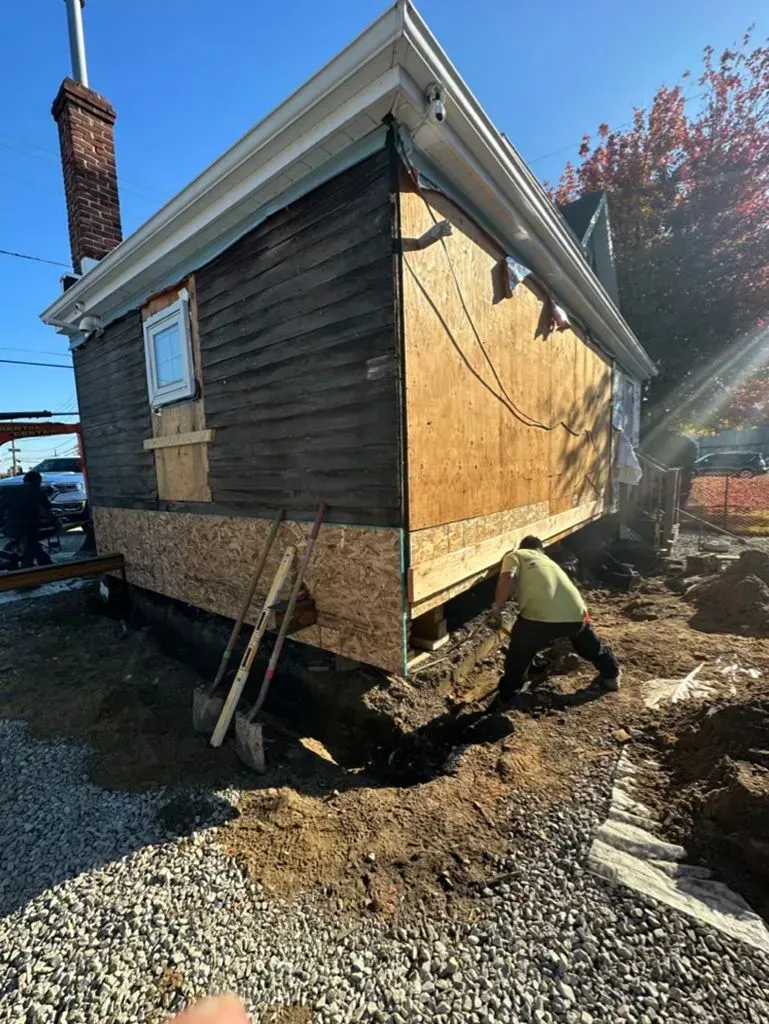 Side view of a small house with new plywood sheathing and a stone foundation on a gravel lot