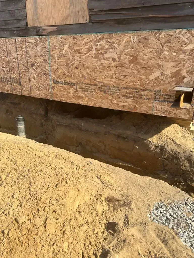 House foundation with wood siding, exposed soil, and gravel in a construction area