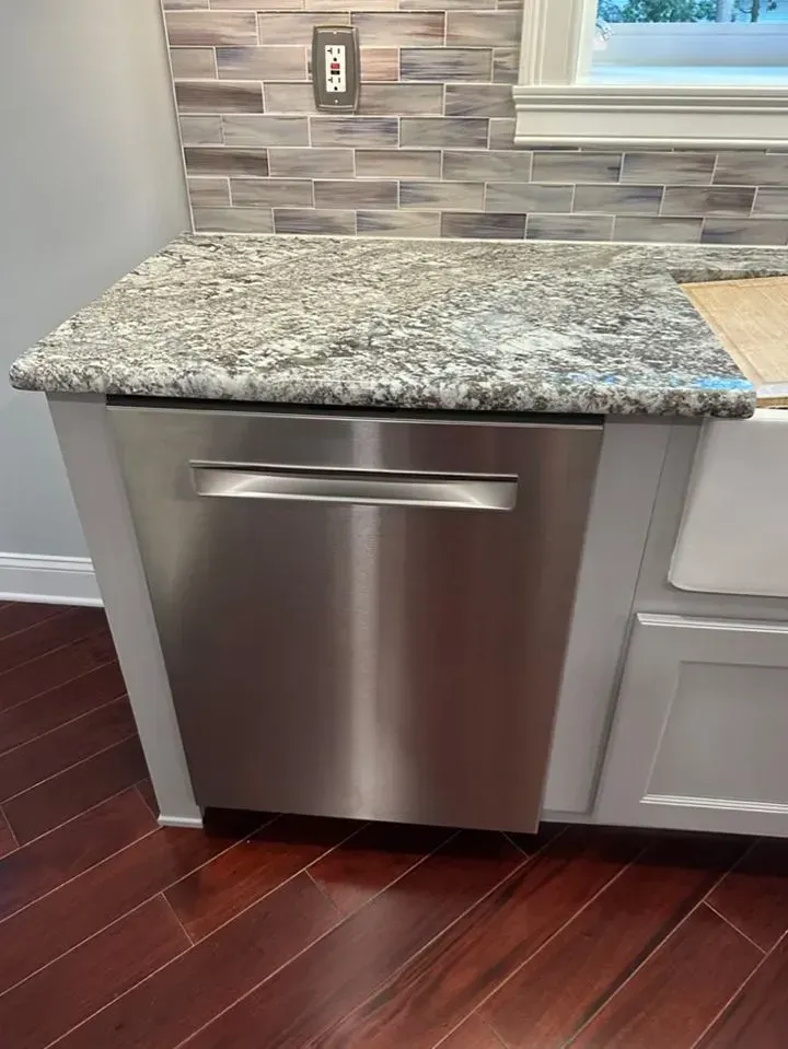 Stainless steel dishwasher under granite countertop in a kitchen with dark wood floor and tile backsplash