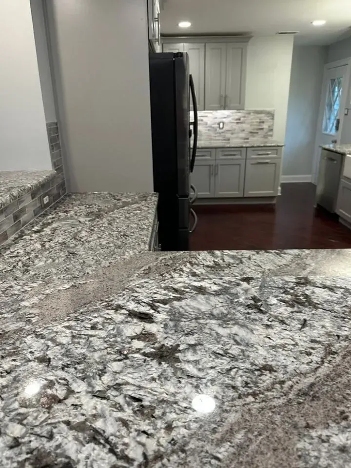 Granite kitchen countertops with dark wood cabinets and stainless refrigerator in a bright kitchen