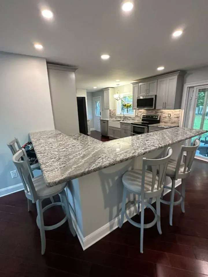 Bright kitchen with gray granite island, white bar stools, recessed lights, and dark wood floors