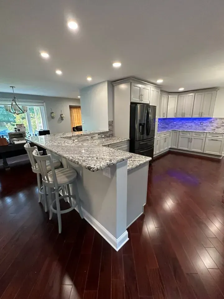 Modern kitchen with granite island, bar stools, dark wood floors, stainless fridge, and blue under-cabinet lighting