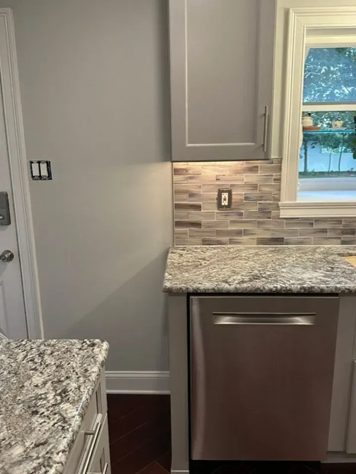 Modern kitchen with granite counters, gray cabinets, tiled backsplash, and a window over a stainless dishwasher.