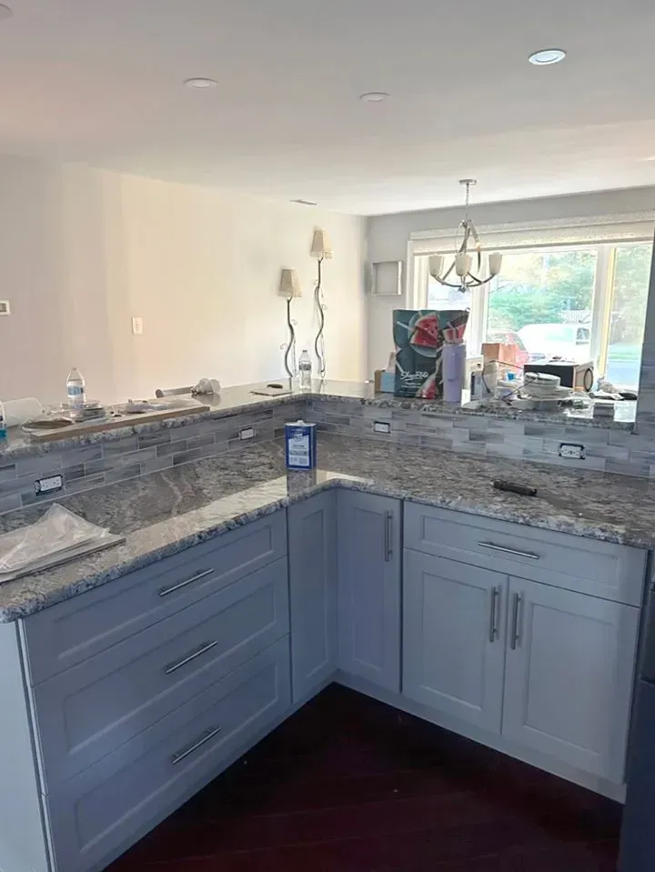 Corner kitchen with blue-gray cabinets, granite countertops, and a sink overlooking a bright dining area.