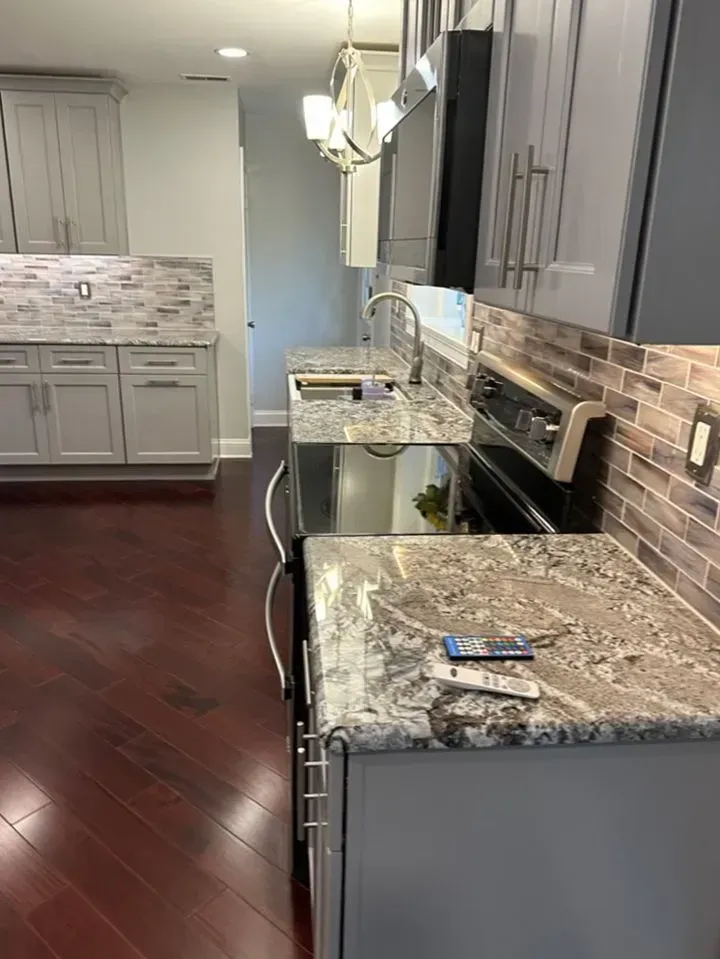 Modern kitchen with dark wood floors, gray cabinets, marble counters, and a black stove
