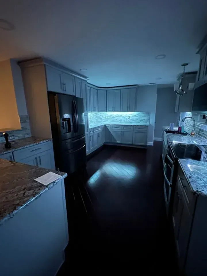 Dim modern kitchen with dark floors, white cabinets, black appliances, and a bright window seat.
