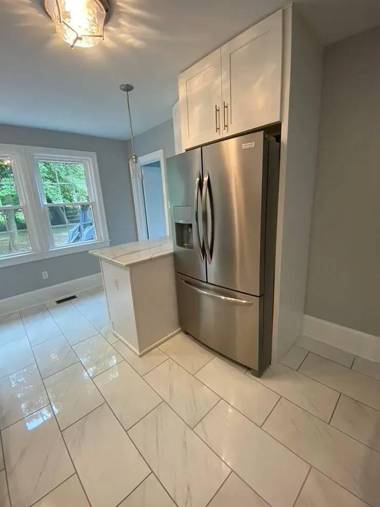 Bright kitchen with stainless steel fridge, white cabinets, tile floor, and window by the counter.