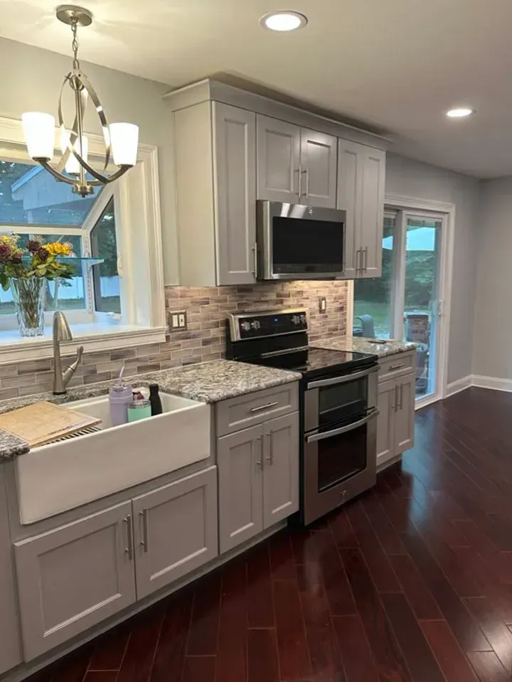 Modern kitchen with gray cabinets, stainless appliances, white counters, and dark wood floors.